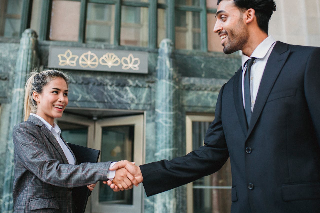 gallery-4 Two business professionals shaking hands confidently outside a modern building.