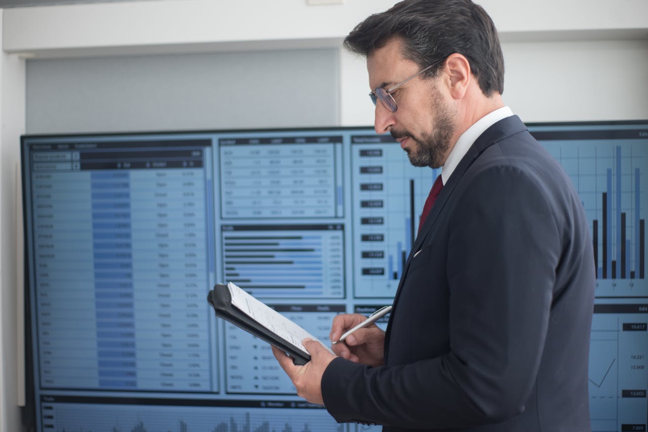 gallery-6 Businessman in a suit analyzing data analytics on large screens, taking notes.